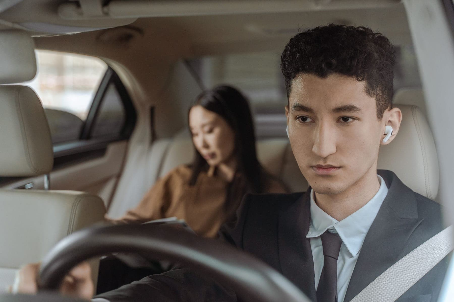 A suited close protection officer with an earpiece driving a client